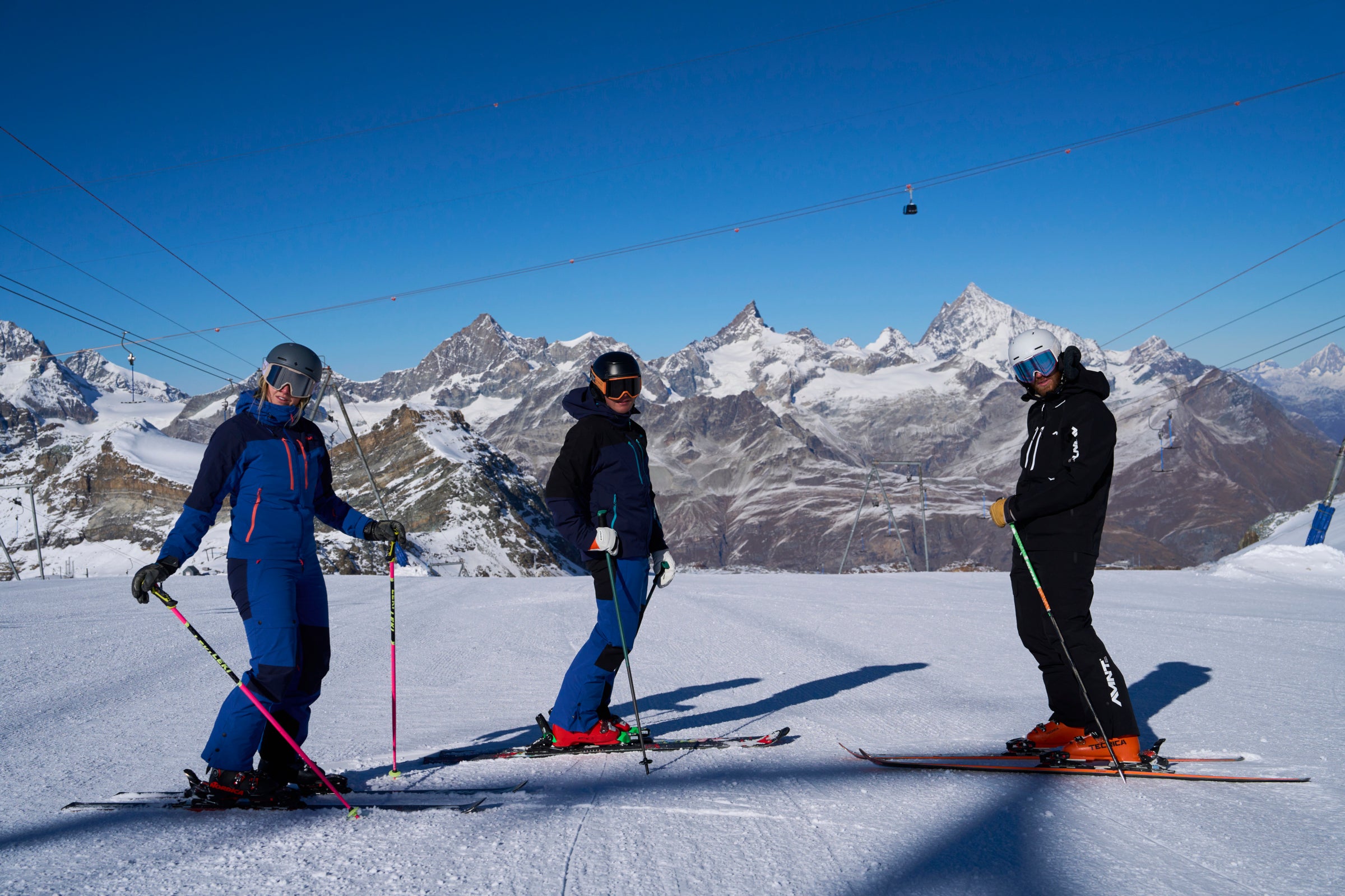 Three skiers standing on a snowy slope with mountain peaks behind